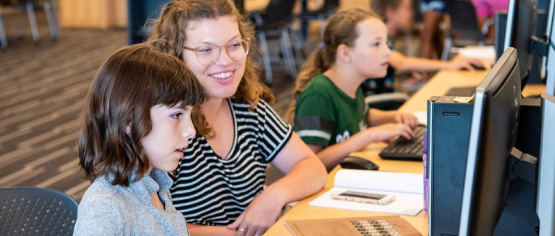 A college teaching apprentice and students typing on computers.